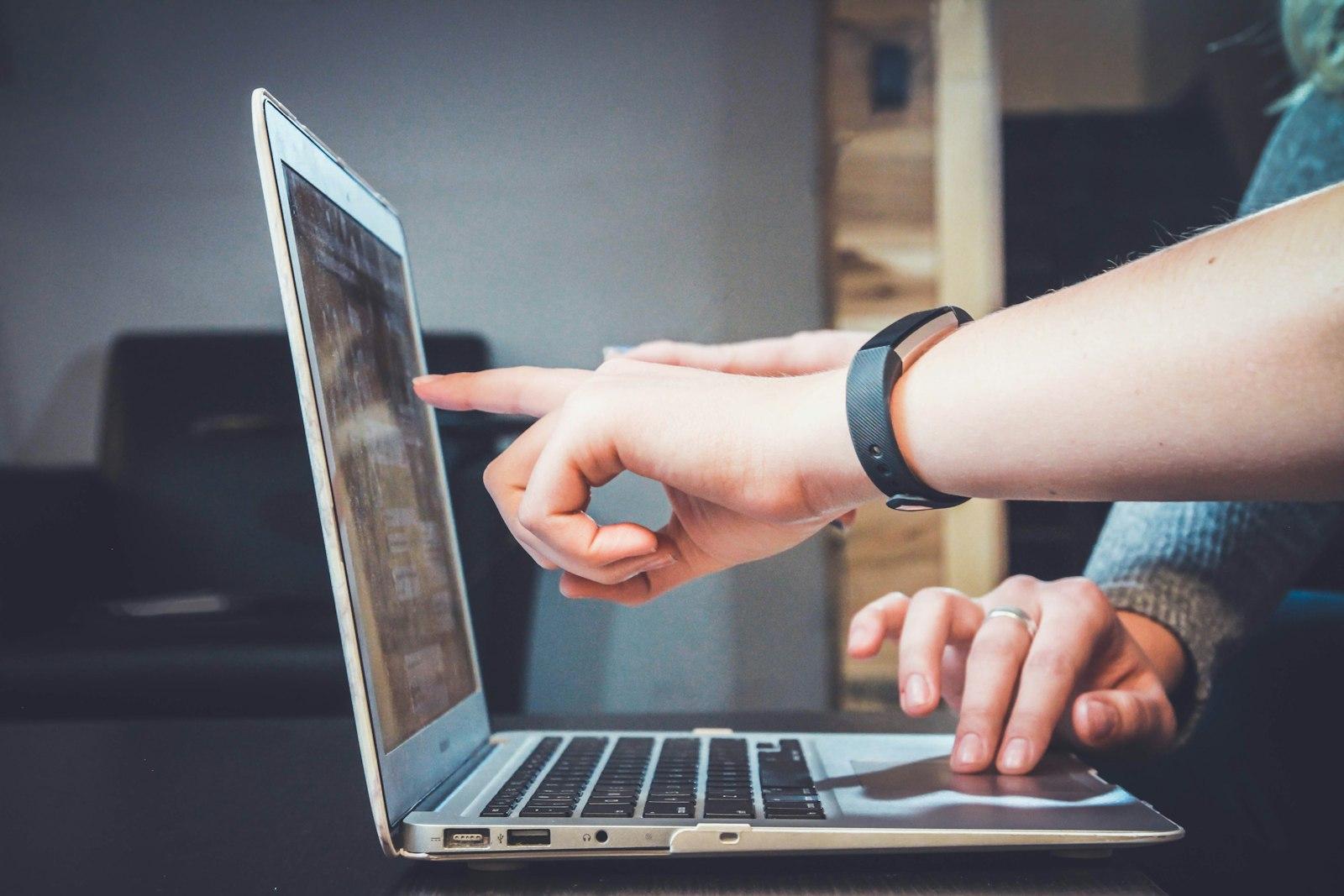 A hand pointing at a laptop screen while reviewing content