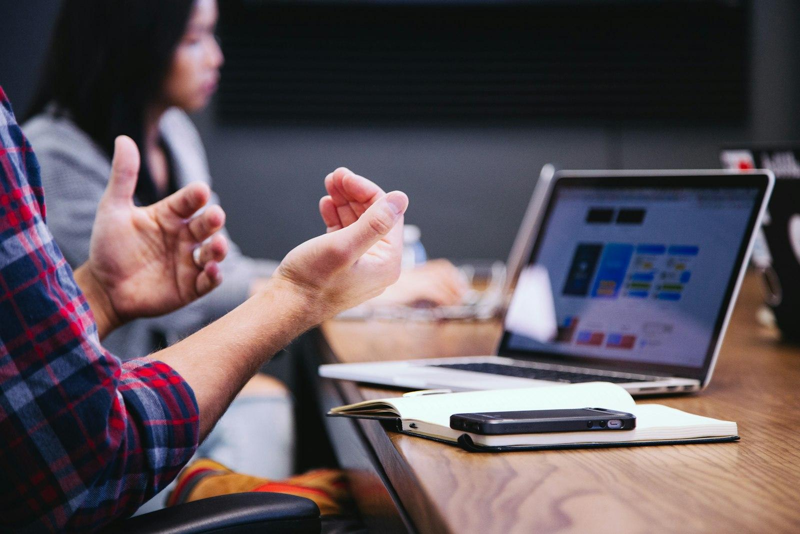 A person gesturing while explaining a report on a laptop in a meeting